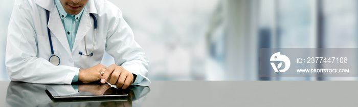 Male doctor sitting at table with tablet computer in hospital office. Medical healthcare staff and doctor service.