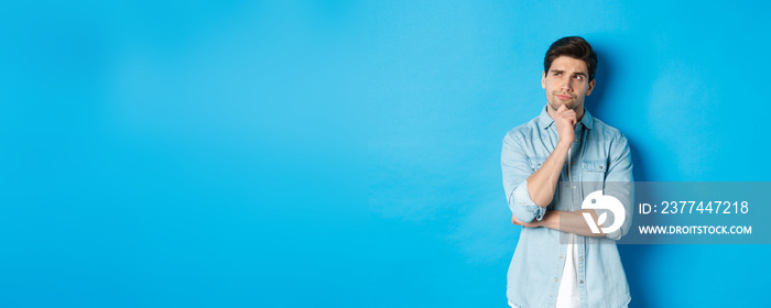 Image of adult bearded man 25s years, thinking about something, looking at upper left corner and pondering ideas, standing over blue background