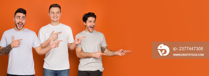 Male friends pointing fingers at copy space on orange background