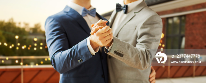 homosexuality, same-sex marriage and lgbt concept - close up of happy male gay couple holding hands and dancing on wedding over roof top party background