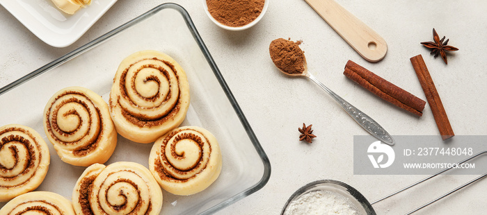 Baking dish with uncooked cinnamon rolls and ingredients on light background