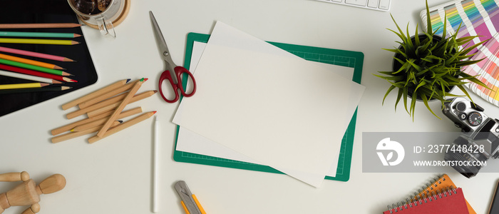 Designer workspace with sketch paper, painting tools, camera, supplies and decoration on white table