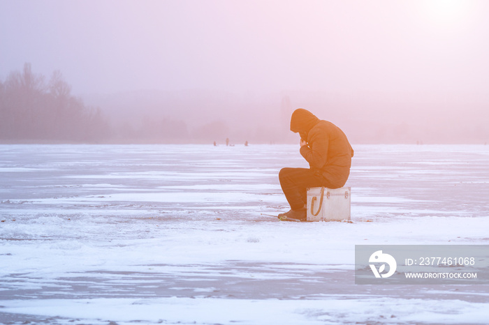 A fisherman on winter fishing on a frosty evening sits on an ice floe, in the fog, a winter landscape