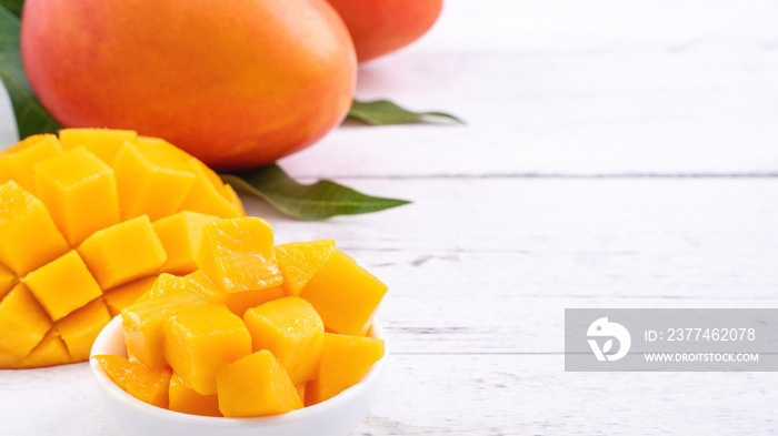 Fresh mango,beautiful chopped fruit with green leaves on bright wooden table background. Tropical fruit design concept, close up, copy space.