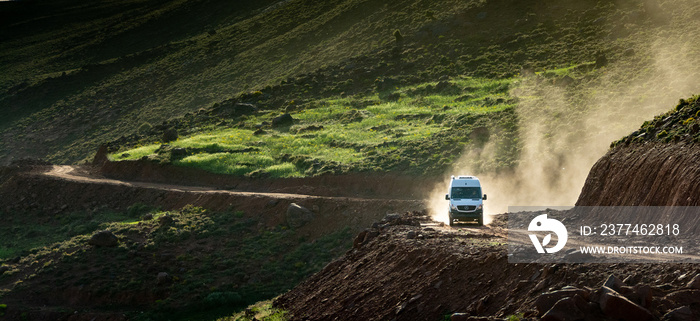 In the Atlas Mountains in Morocco. A 4x4 van lifts a cloud of dust on the dirt road that climbs towards the Tizi N’Tighist in the Ait Boulli valley