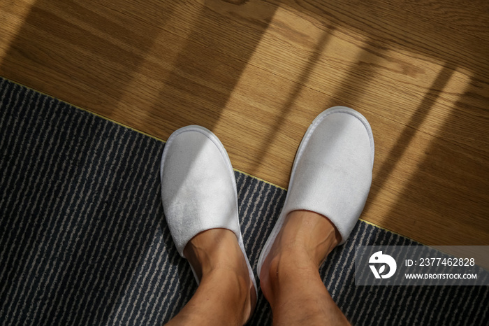 Male feet wearing white hotel slippers, view from above