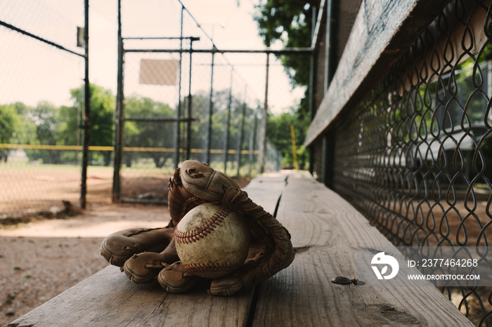 Baseball equipment shows ball and glove on dugout bench at park field for sport.