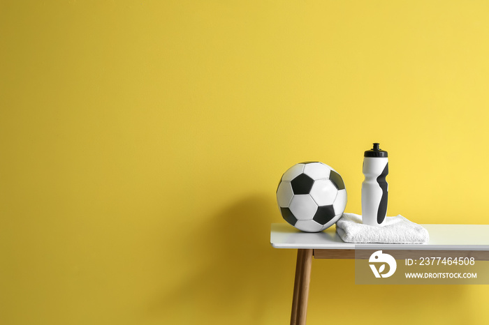 Soccer ball, bottle of water and towel on table near color wall