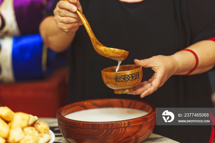 A woman pours  kumis  milk drink into a wooden bowl with an ornament in the national Kazakh style. Central Asian traditional drink on the festive table Nauryz.