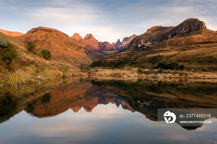 A horizontal shot of mirror-like reflections of a mountain range in a calm lake, taken at sunrise, Cathedral Peak, Drakensberg, South Africa