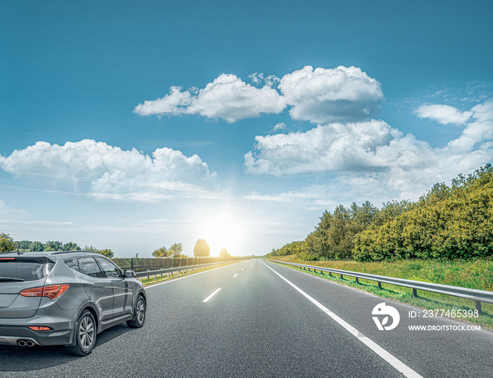 A Black car rushes along the road against the backdrop of a beautiful countryside landscape.