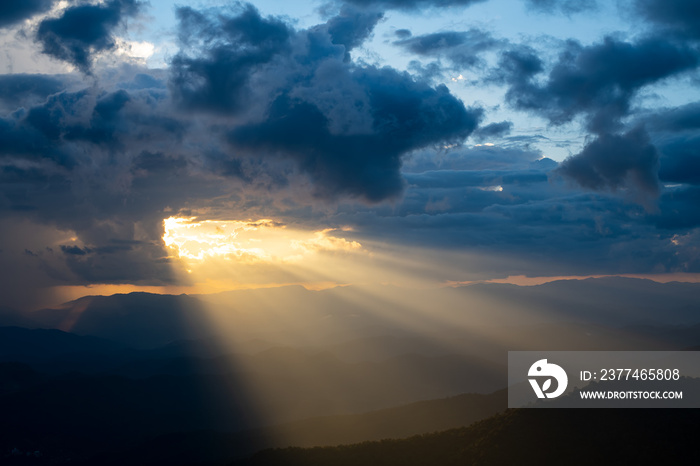 The bright rays of the sun are shining from saturated clouds to mountain range before sunset.