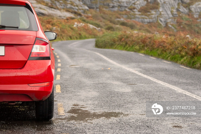 Red small car parked off road. Beautiful nature scenery. Low cloudy sky. Nobody. Wild Atlantic Way rout. Rough stone terrain. Transport and travel concept.