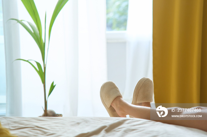 Child in warm slippers and socks lying down on the bed by the window. Lazy day off warm place concept