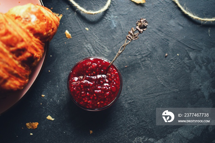 Raspberry jam in a glass bowl. Beautiful silver spoon with raspberry jam. Tasty jam on a dark background.