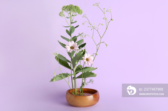 Bowl with beautiful ikebana on lilac background