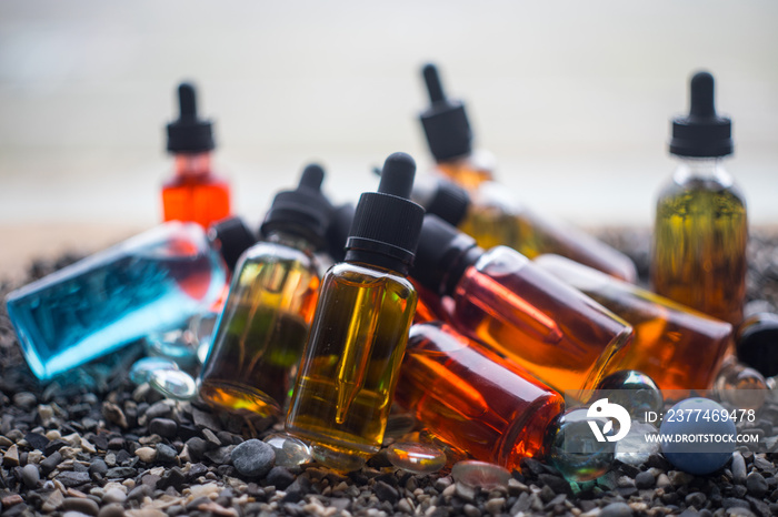 Vape concept. Beautiful colorful vape liquid glass bottles outdoor on stones. Useful as background or electronic cigarette advertisement.