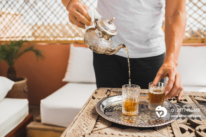 Man holding in hand silver vintage teapot and pouring traditional mint sweet moroccan tea. Arabian hospitality and service.