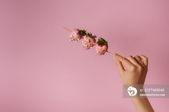 A girl holds strawberries covered in chocolate on a pink background