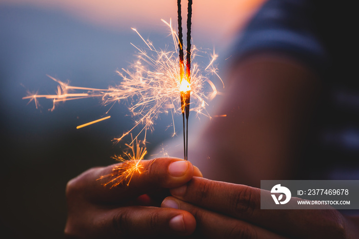 Woman holding and playing with fire sparklers on the festival in the rice field at sunset time