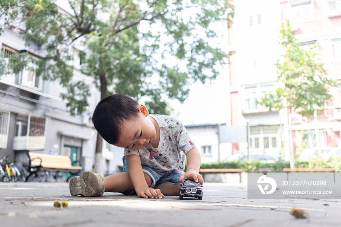 一个小男孩坐在院子里玩玩具车