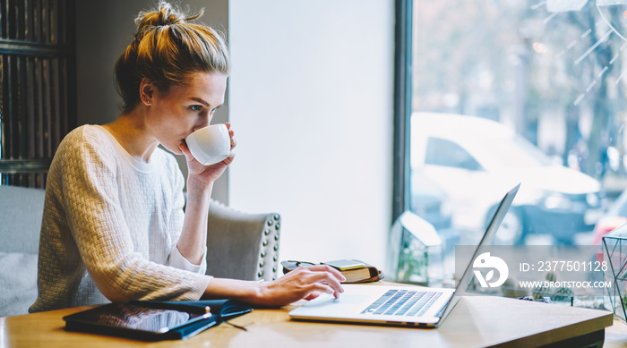 Concentrated creative copywriter drinking tasty coffee while working remote at modern laptop compute