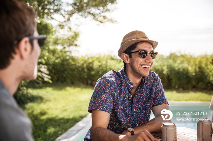 Young man sitting with friends by poolside laughing