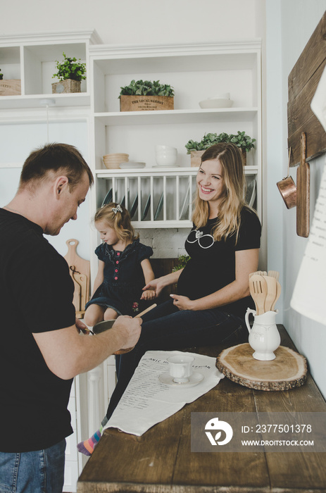 一个年轻的家庭，带着孕妇和小女孩坐在斯堪的纳维亚厨房里玩得很开心