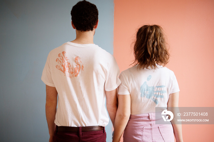 Couple standing against wall holding hands in matching t-shirts