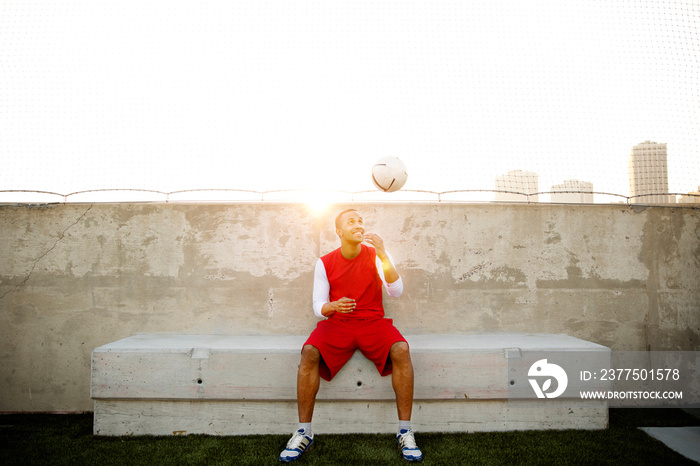 Portrait of young man sitting on bench and playing with soccer ball