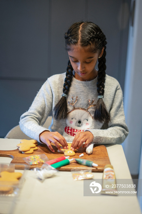 Girl decorating gingerbread cookies in kitchen