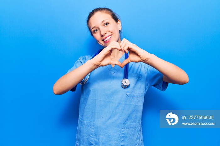 Young blonde woman wearing doctor uniform and stethoscope smiling in love showing heart symbol and s