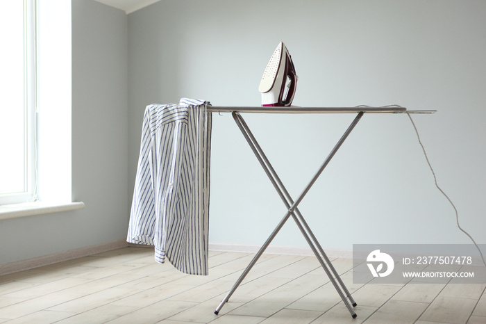 Iron and ironing board in a bright room. Iron clothes.