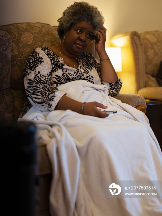 Woman sitting under blanket and watching TV