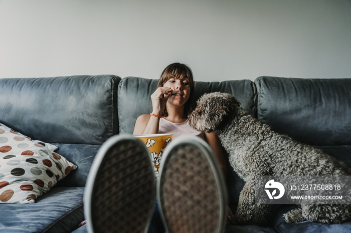 年轻女孩和她漂亮的棕色西班牙水犬度过了一个有趣的下午。坐在沙发上吃东西