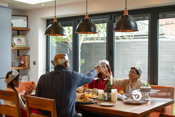 Family wearing paper crowns toasting during Christmas dinner