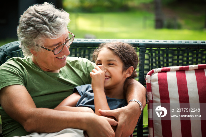 Smiling grandfather and granddaughter sitting on bench outdoors