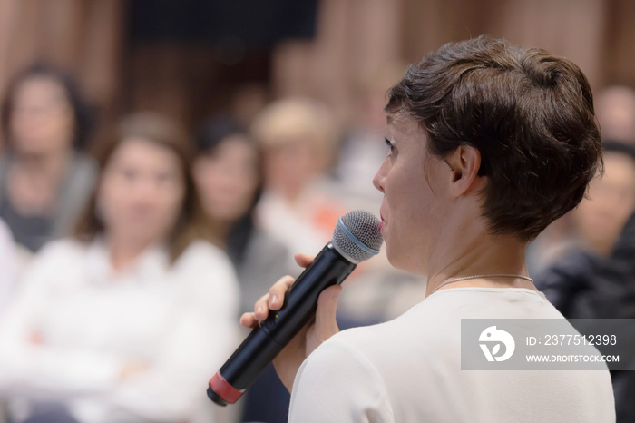 Beautiful business woman with microphone in her hand speaking at the  conference or seminar.