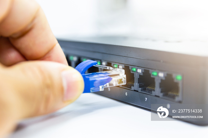 Hand of man holding The blue network cables connect port switch on white table concept internet netw