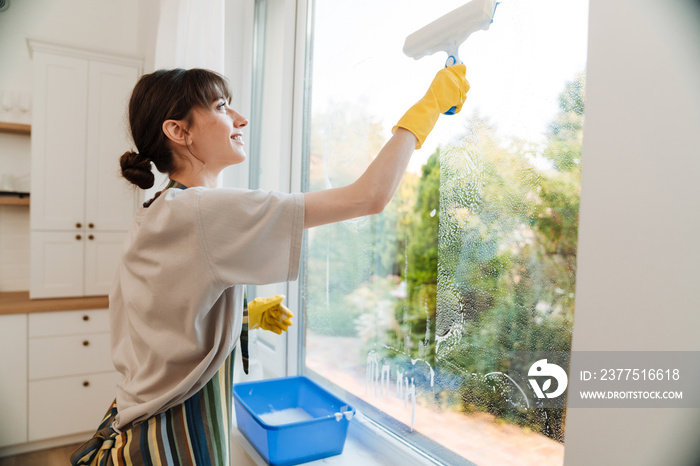 White young woman in gloves smiling while cleaning window