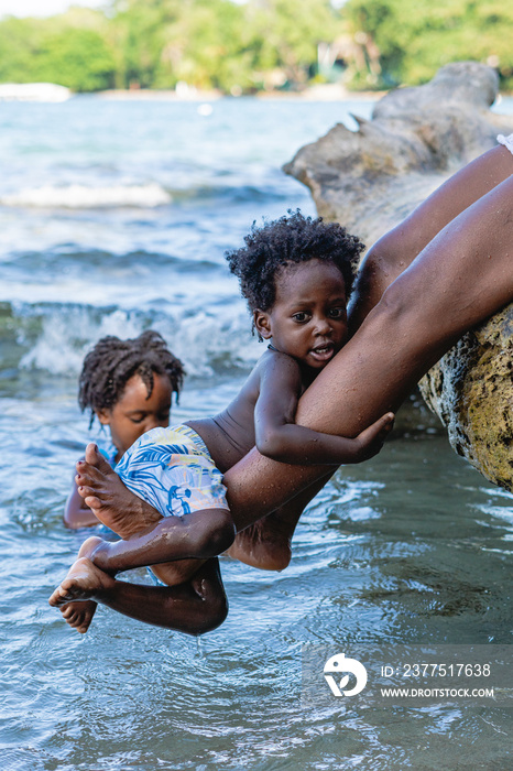 Imagen vertical  de un pequeño niño afroamericano de cabello afro  jugando abrazado a las piernas de