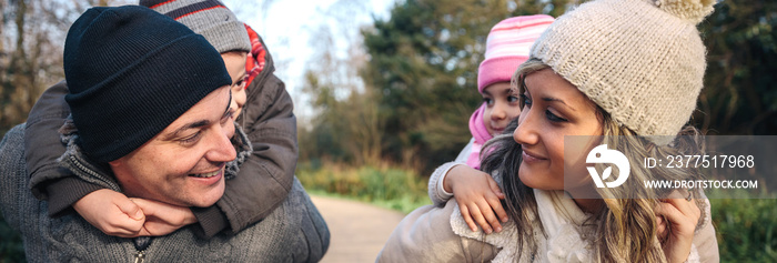 Portrait of smiling parents giving piggyback ride to happy children over a wooden pathway into the f