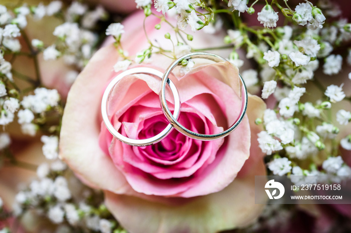 Wedding bouquet with pink roses on wooden table with rings.