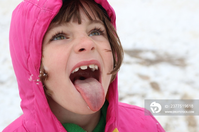 Portrait of a young girl in the snow trying to catch a snowflake on her tongue