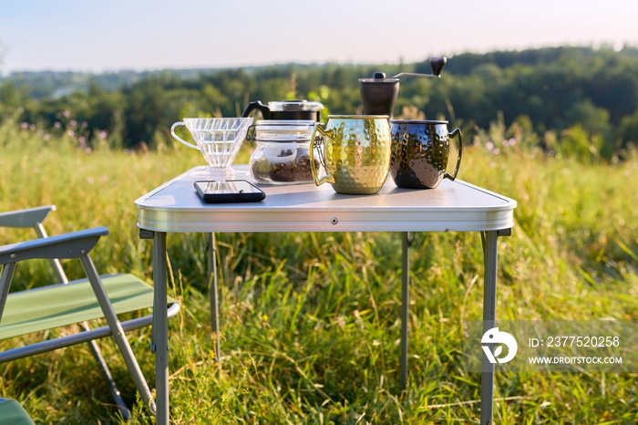 Mugs, grinder, coffee beans on folding table for outdoor camping