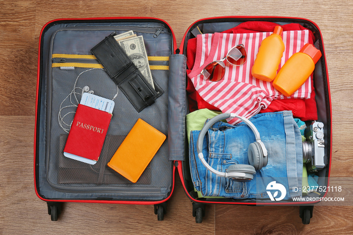 Open suitcase with travel accessories on wooden floor