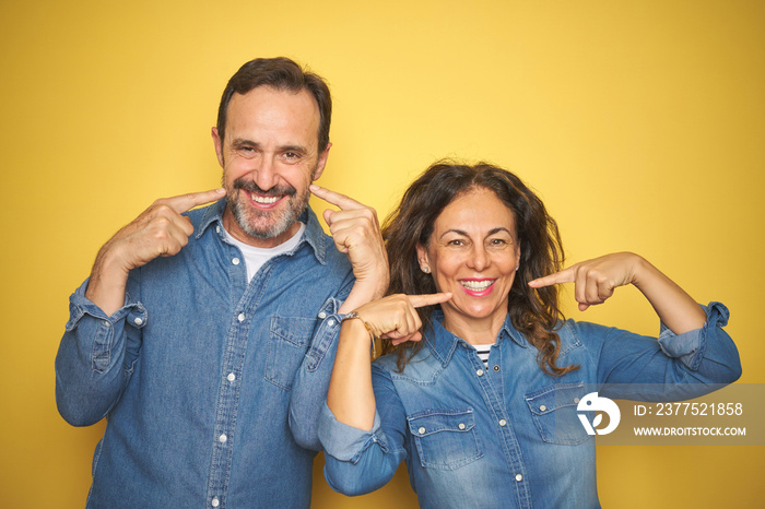 Beautiful middle age couple together standing over isolated yellow background smiling cheerful showi