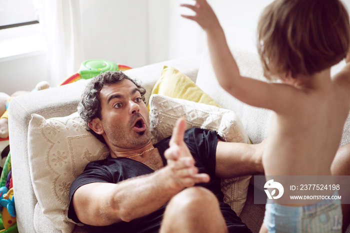 Father playing with his daughter on sofa at home