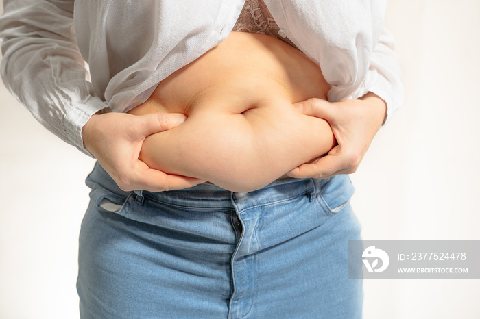 overweight woman holding fold of excess fat on stomach