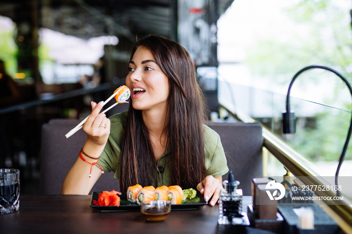 Young woman eating and enjoying fresh sushi in luxury restaurant. Female client holding food sticks 